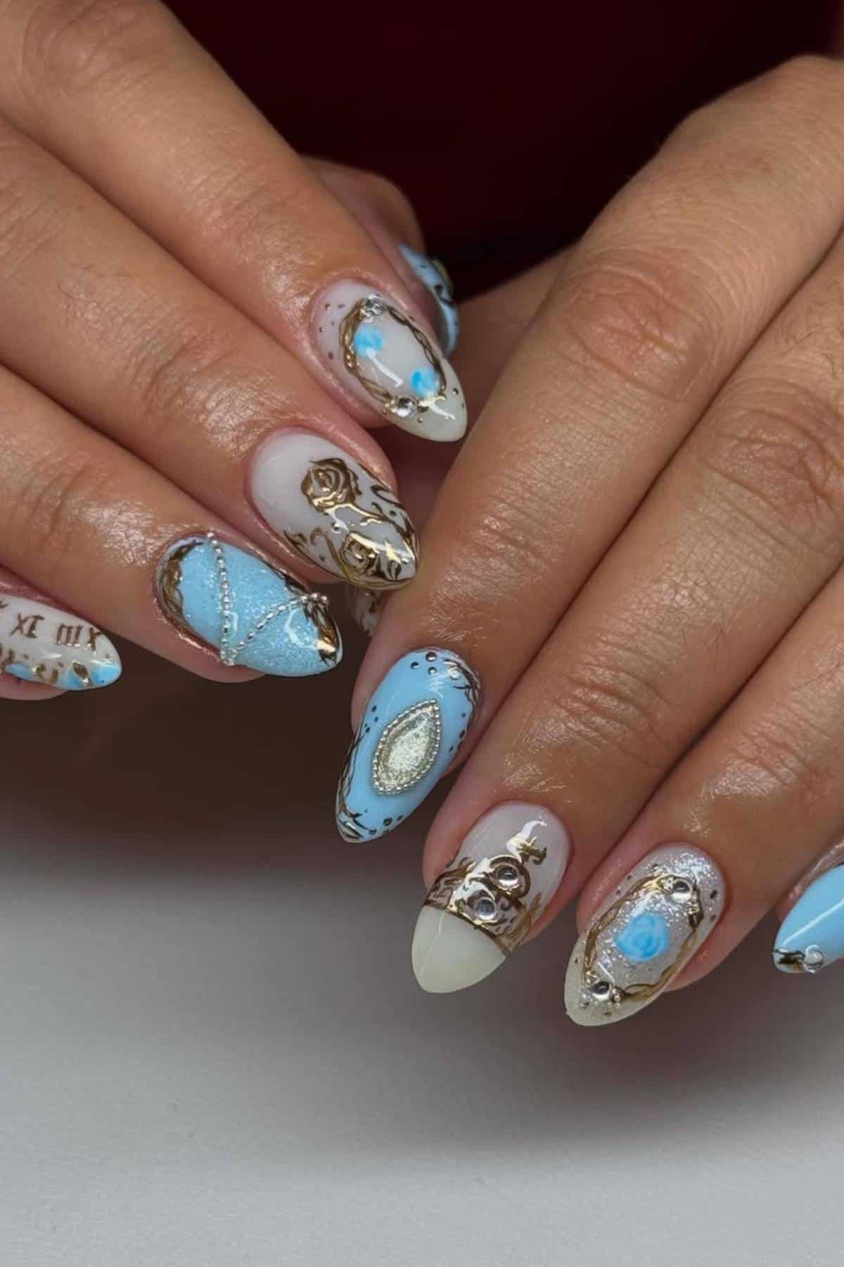 Hands with long, almond-shaped nails featuring intricate blue, gold, and white designs, including jewels, clock motifs, pearls, and painted patterns.