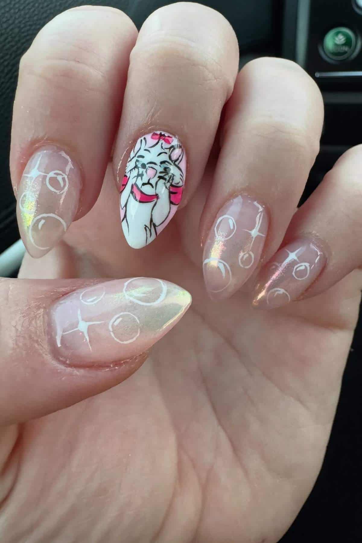 A hand with almond-shaped nails painted with a translucent pink base, white bubble designs, and a cartoon cat face with a pink bow on the ring fingernail.