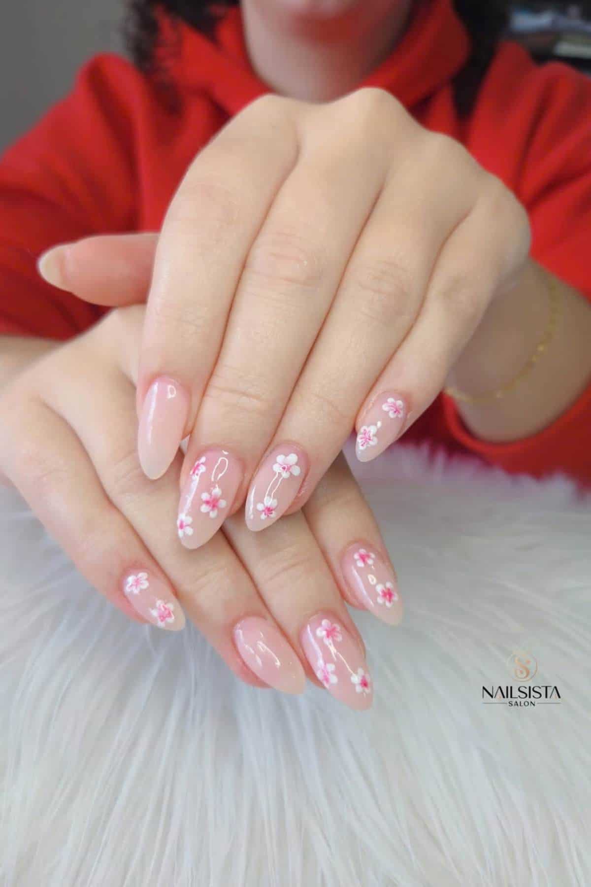 A person with manicured nails featuring a light pink base and small white and pink floral designs, hands resting on a white furry surface.