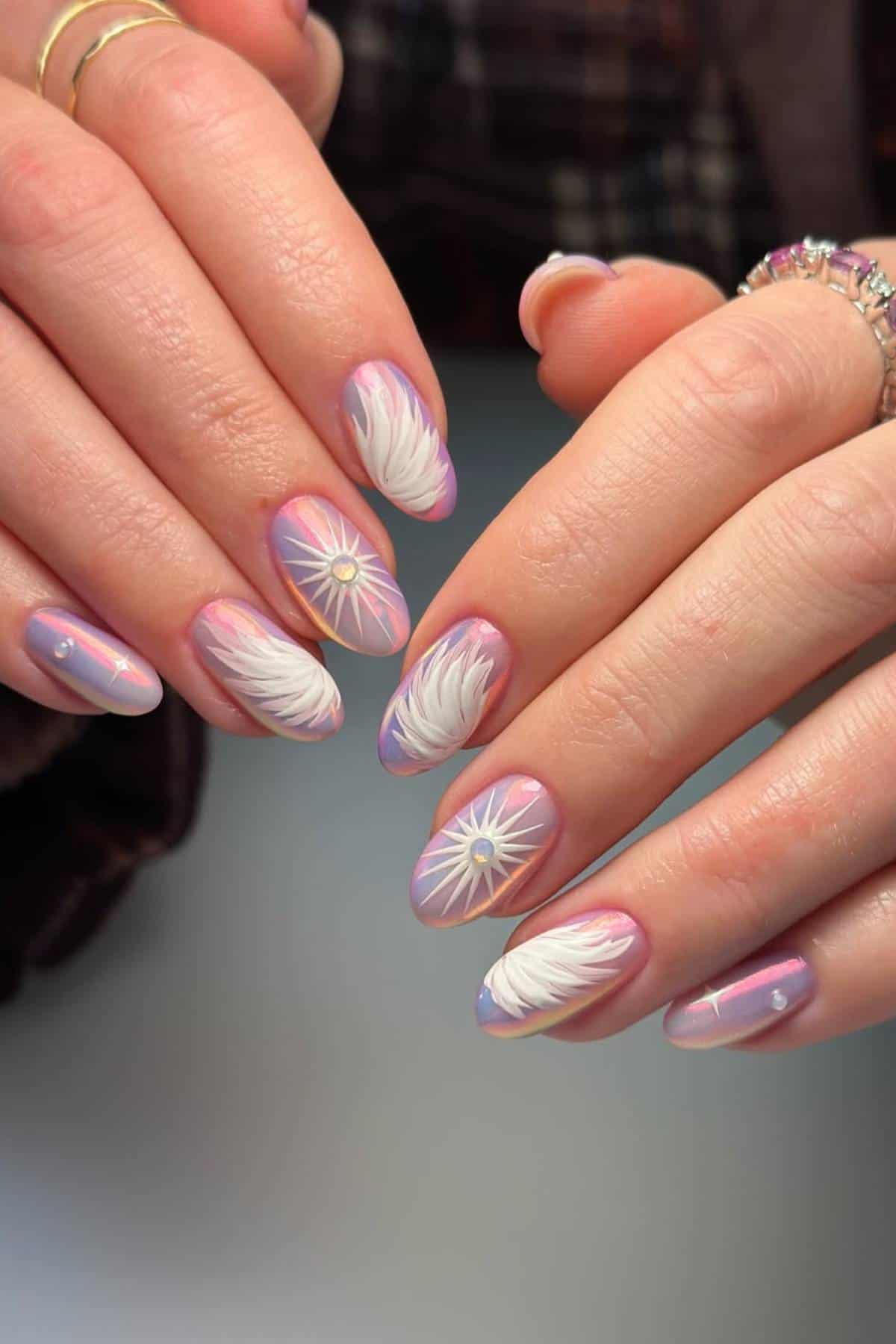 Hands with long almond-shaped nails painted with a pastel gradient and decorated with white feather designs and small pearl accents.