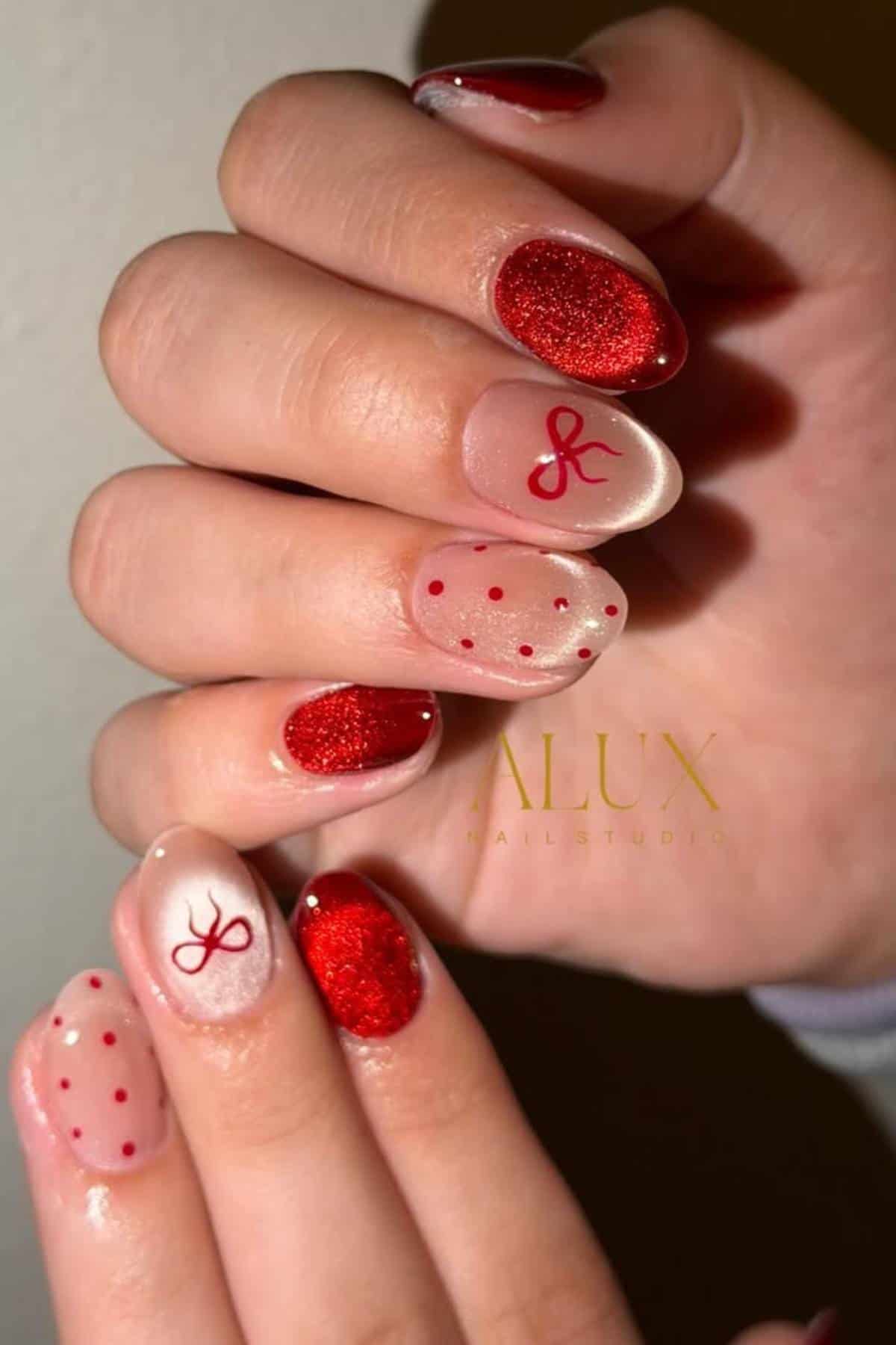 Close-up of hands with manicured nails featuring red glitter, red polka dots, and a red ribbon design on a light background.
