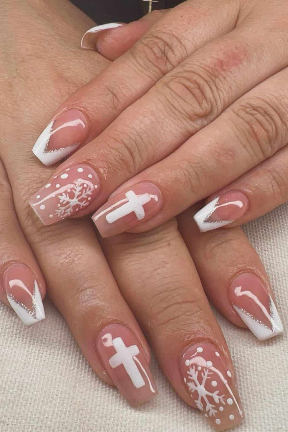 Hands with manicured nails featuring white French tips, a cross design, snowflakes, and polka dots on a neutral pink base.