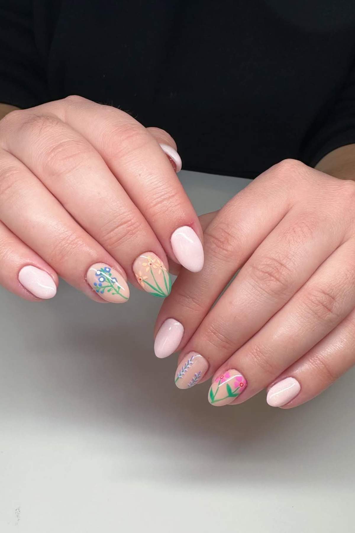Hands with light pink, almond-shaped nails; some nails feature detailed floral designs in various pastel colors.