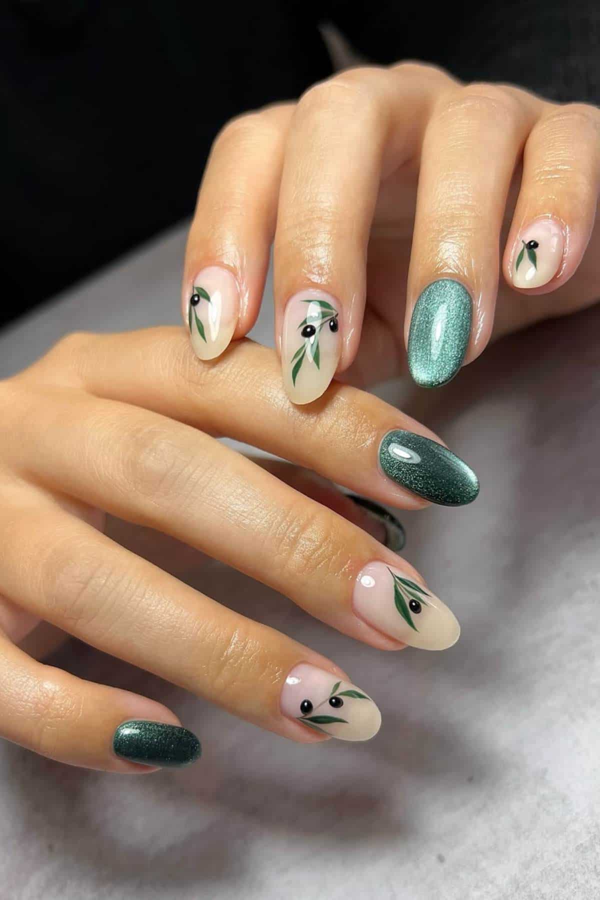 Hands with almond-shaped nails featuring green shimmer polish and nude polish with minimalist green leaf and black dot designs.