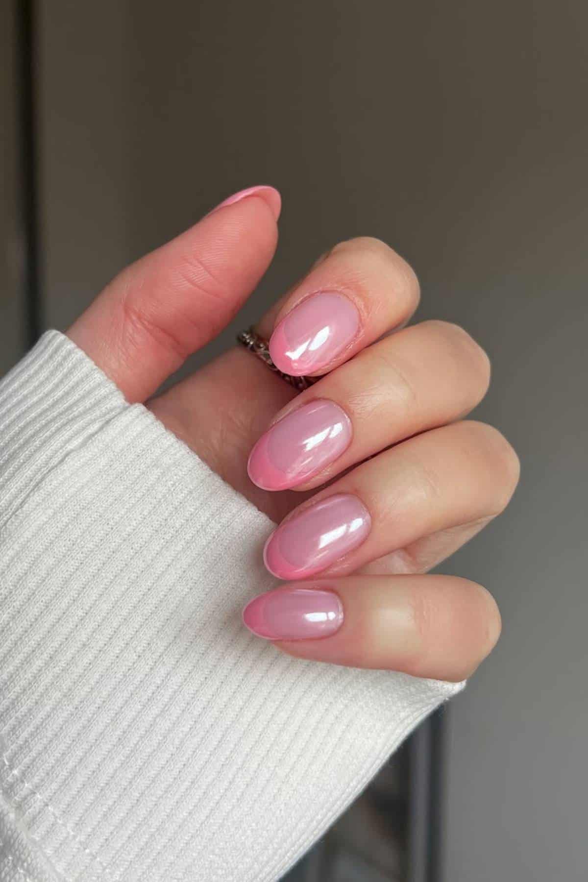 A hand with almond-shaped nails painted with glossy pink nail polish, partially covered by a white sweater sleeve.