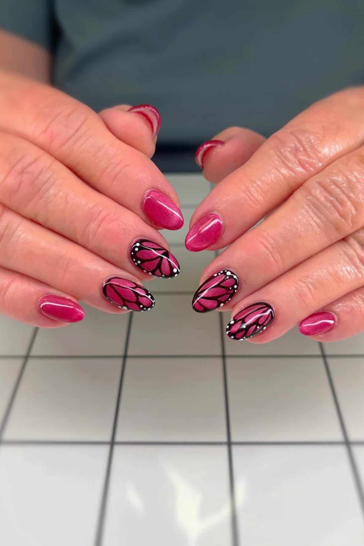 Hands with pink manicured nails; two nails on each hand feature butterfly wing designs with black and white detailing.
