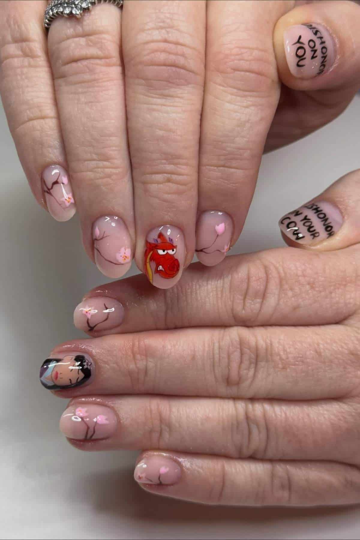 Hands with nude-colored nail polish featuring pink cherry blossoms, cartoon faces, and the phrase "SHOW ON YOU" written on two nails.
