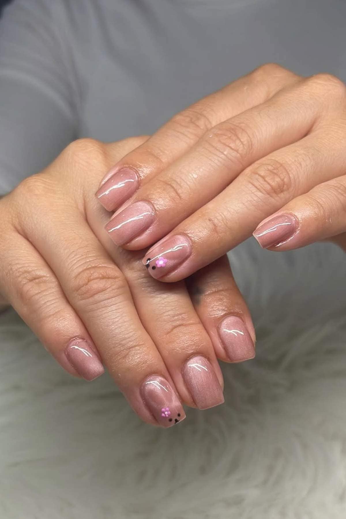 Hands with short, square-shaped nails painted in a pale pink polish, with small black and pink dot accents on the ring fingernails.