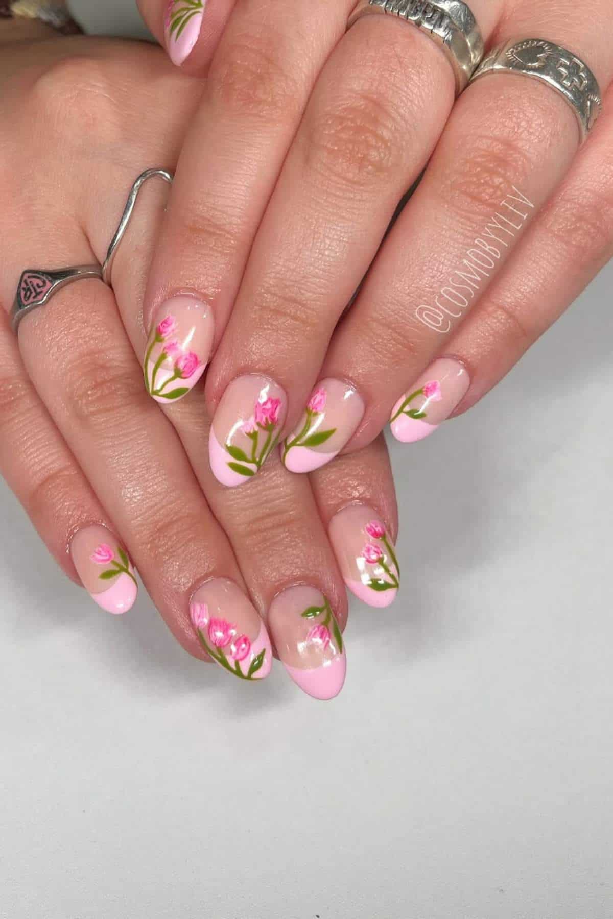 Close-up of hands with almond-shaped nails, featuring light pink tips and small painted pink flower designs with green stems.