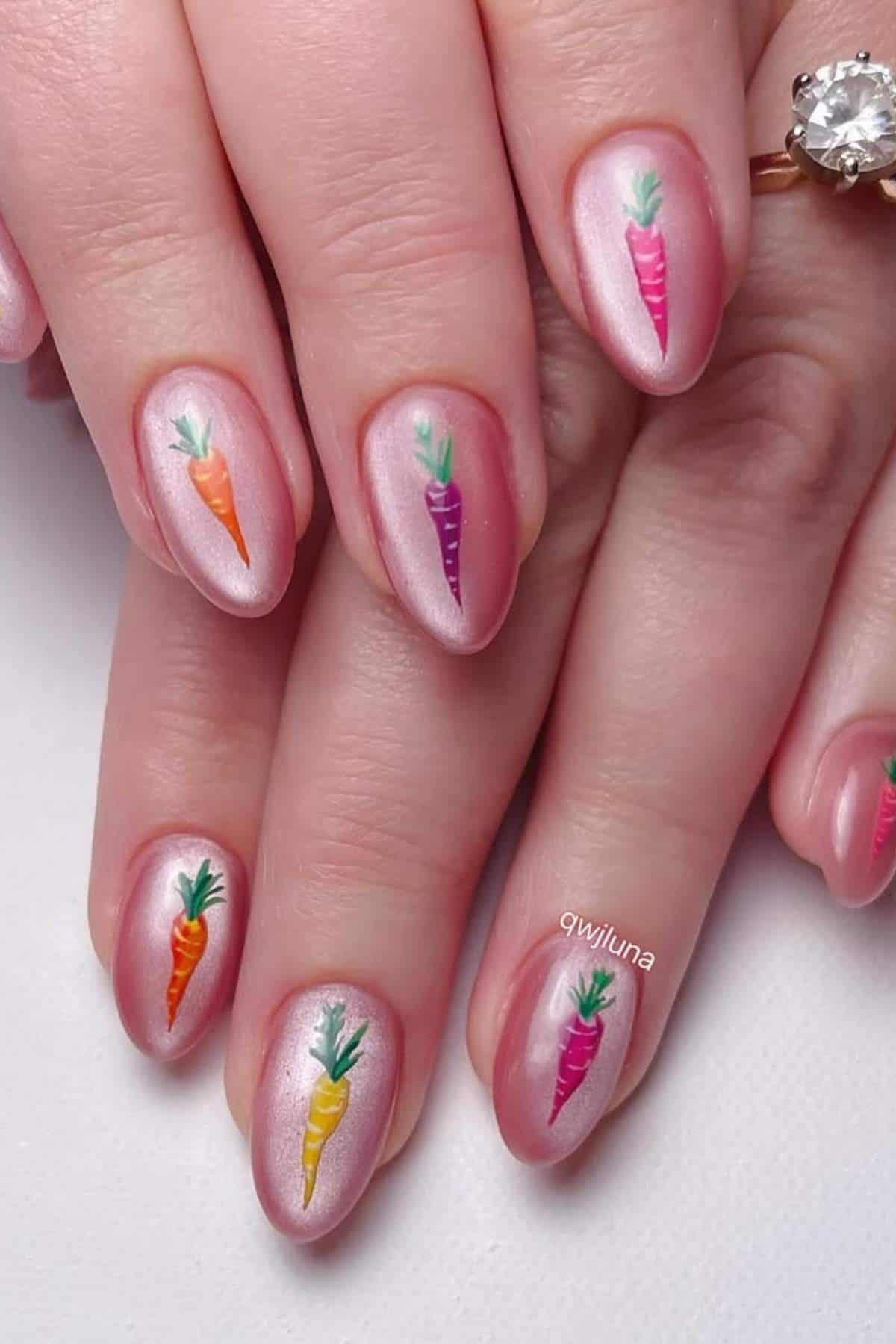 Fingernails with a shimmery pink polish, each featuring a small, colorful carrot design near the tip.