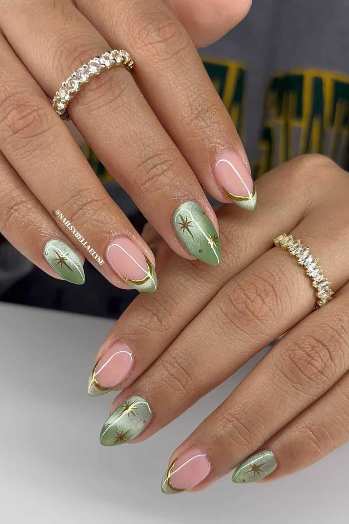 Hands with almond-shaped nails featuring green French tips, gold star accents, and gold rings on the fingers.