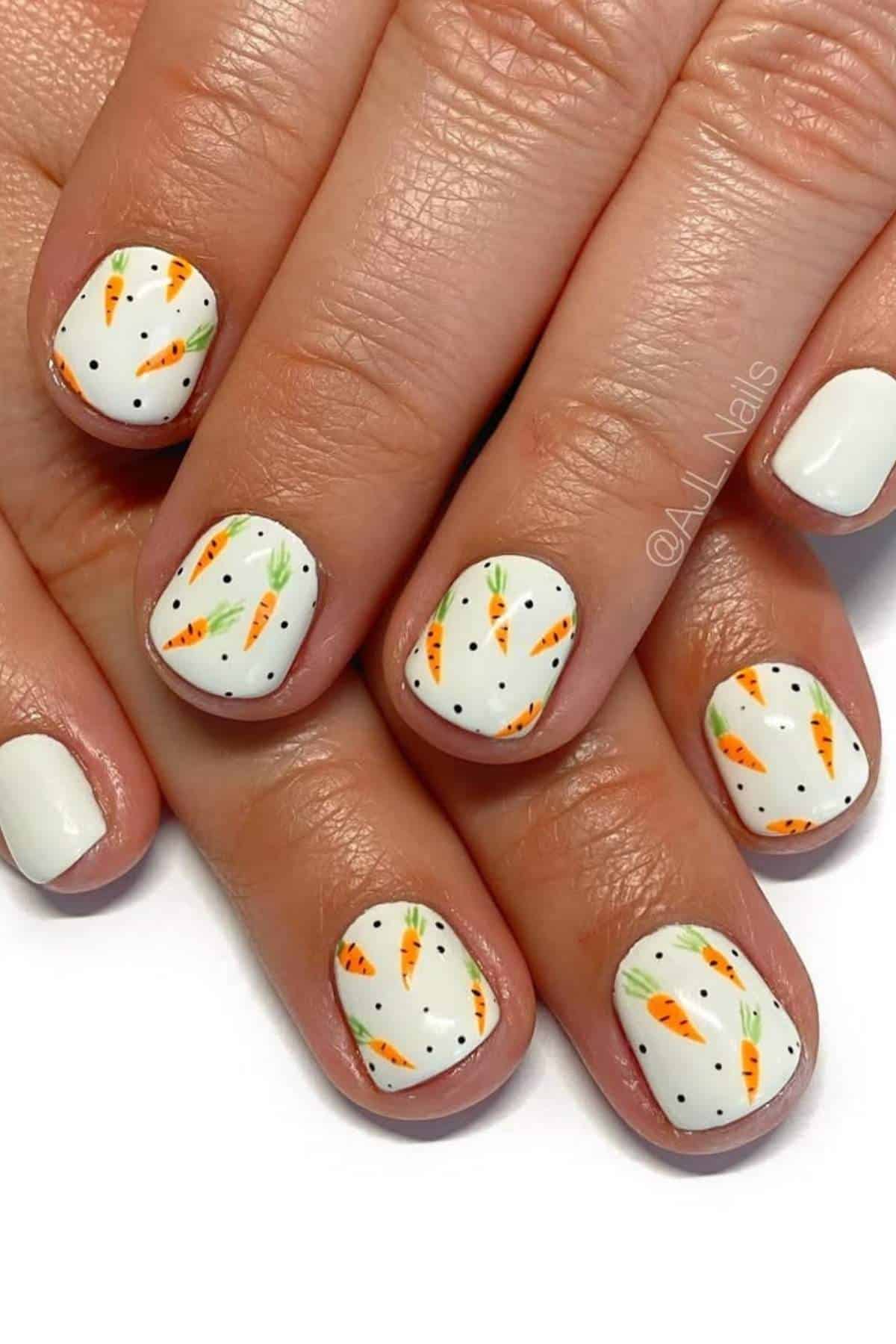 Fingernails painted white with small orange carrot and green leaf designs, shown on both hands with some plain white accent nails.