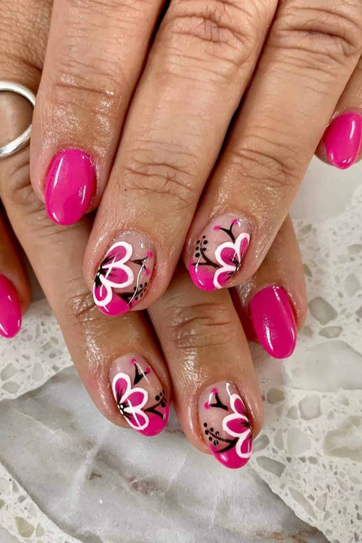 Hands with bright pink nail polish; some nails feature white and black floral designs with small dot accents.