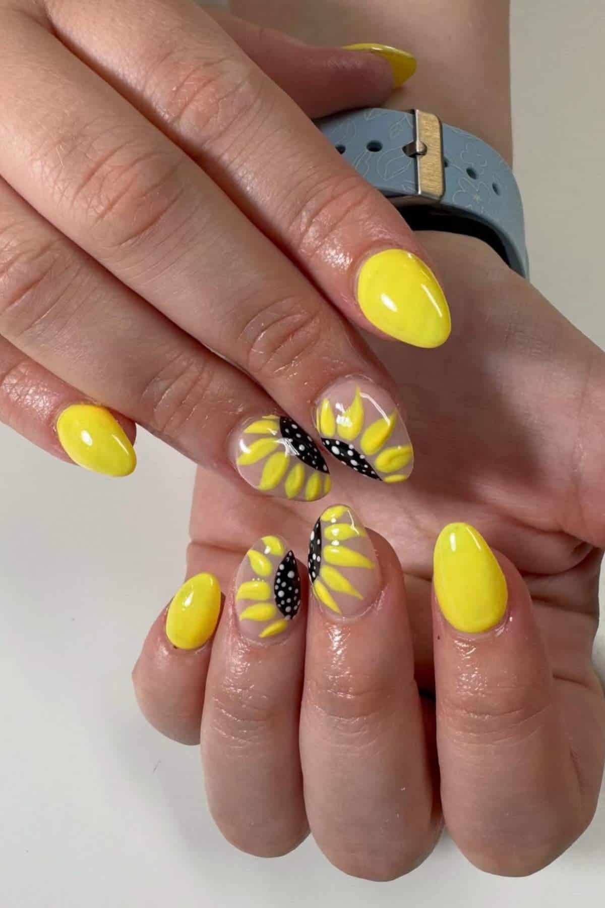 Close-up of hands with almond-shaped nails painted yellow, featuring sunflower designs and black-and-white dotted accents on two nails.