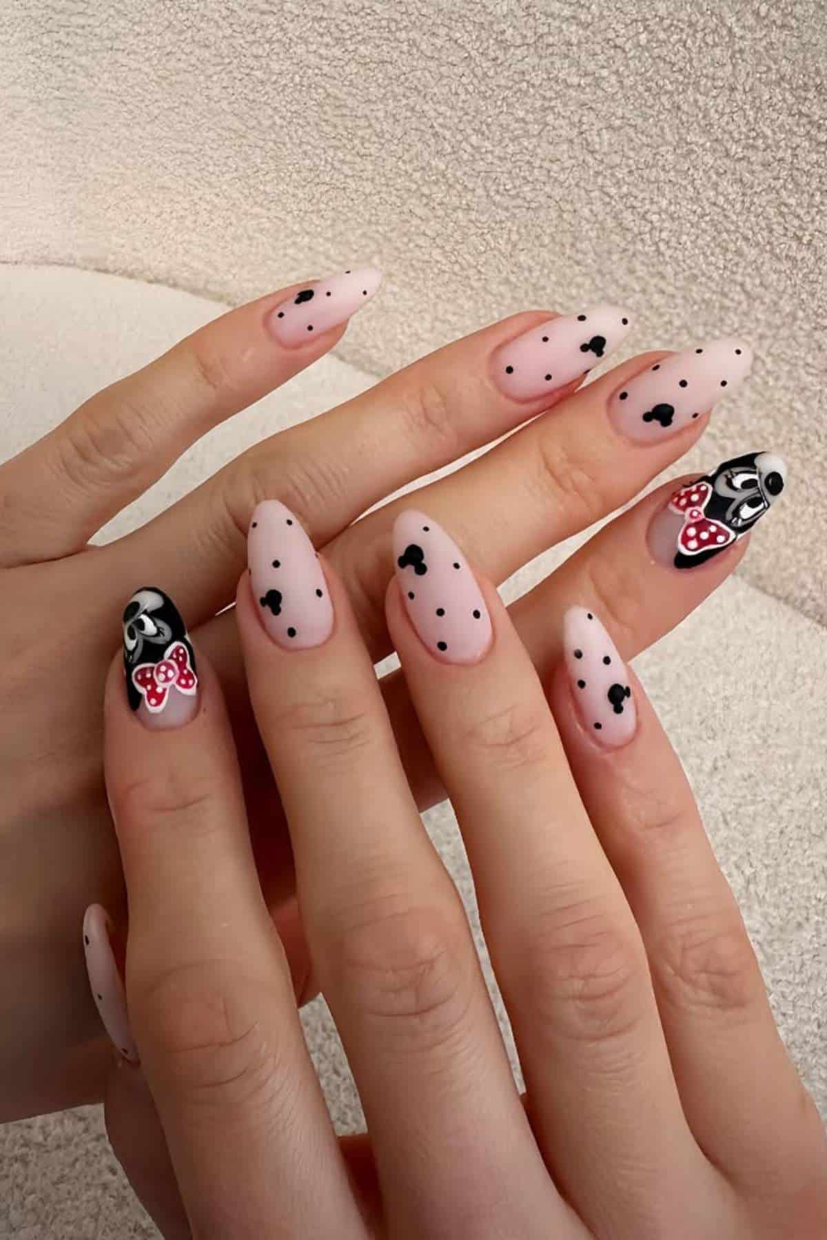 Hands with almond-shaped nails painted light pink, featuring black dots, tiny black Mickey Mouse heads, and detailed Mickey and Minnie Mouse face designs on ring fingers.