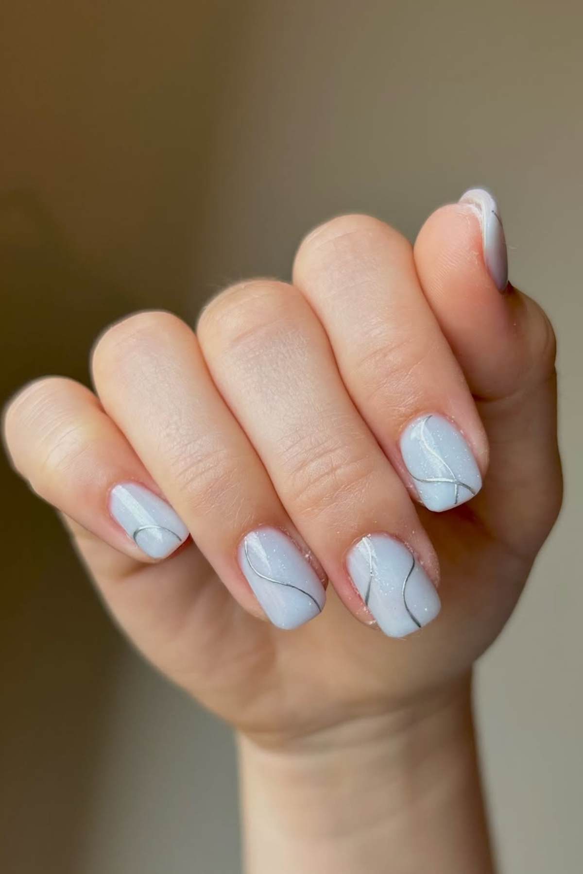 A hand with short, neatly manicured nails painted in pale pastel color with subtle white abstract line designs.