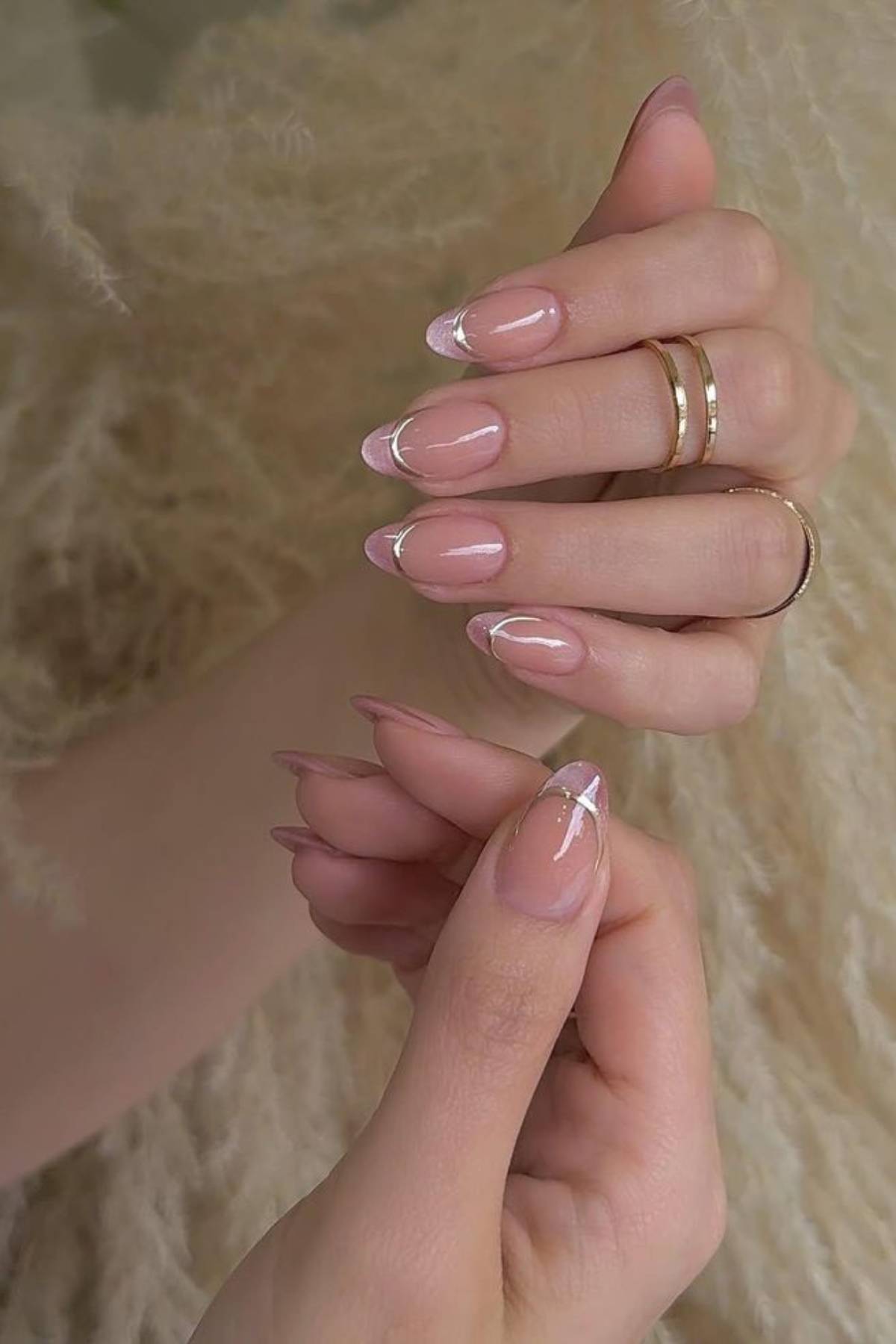 Close-up of hands with almond-shaped nails featuring a minimalist pink and white French tip design. The person is wearing two gold rings on their fingers.