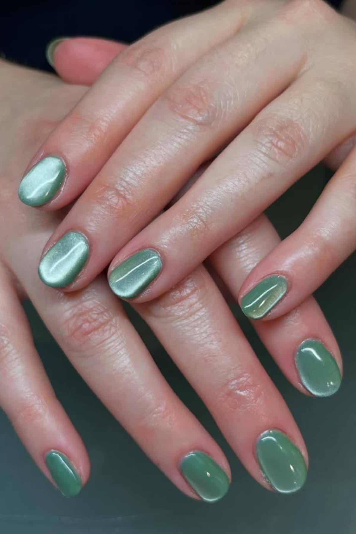Close-up of hands with short, neatly manicured nails painted with glossy, light green nail polish.