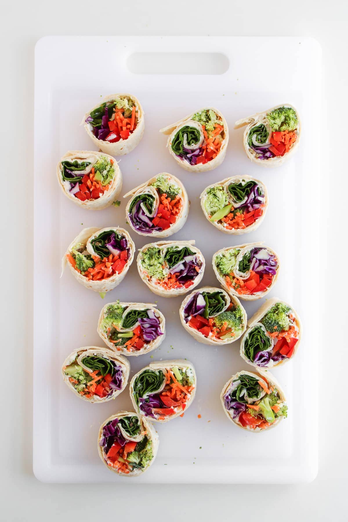 Sliced vegetable wraps arranged on a white cutting board, showing colorful fillings such as lettuce, red cabbage, carrots, and bell peppers.