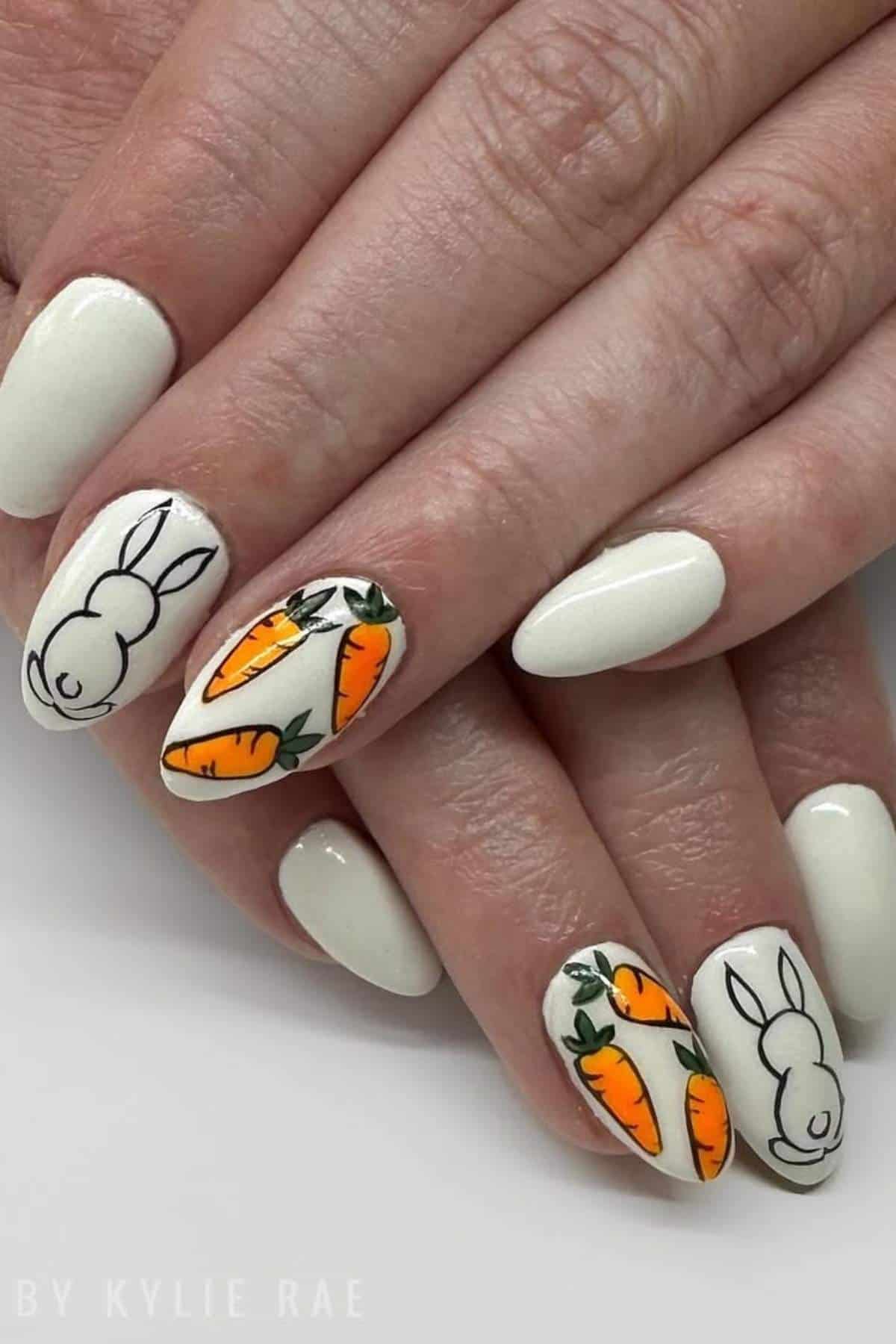 Close-up of hands with white-painted nails, featuring accent nails decorated with carrot and bunny designs.