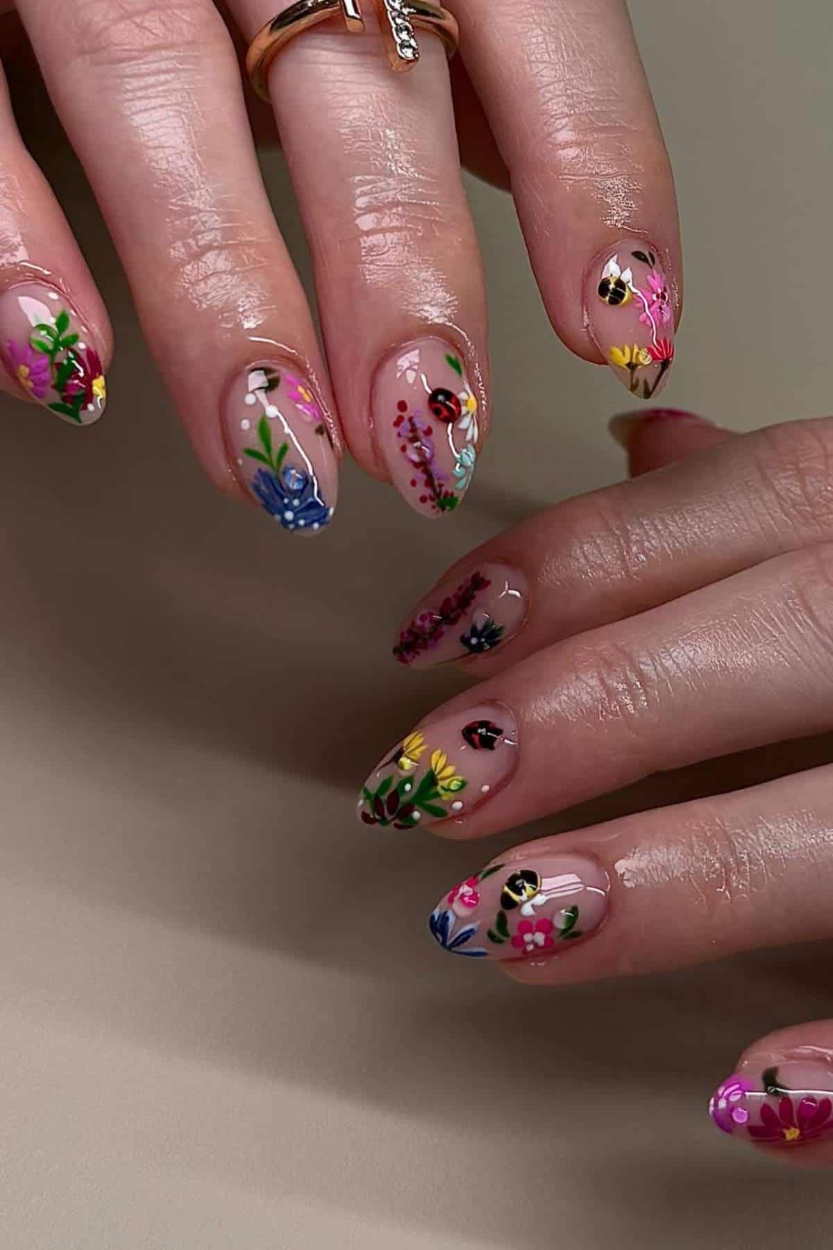 Hands with almond-shaped nails featuring intricate, colorful floral designs on a nude base.
