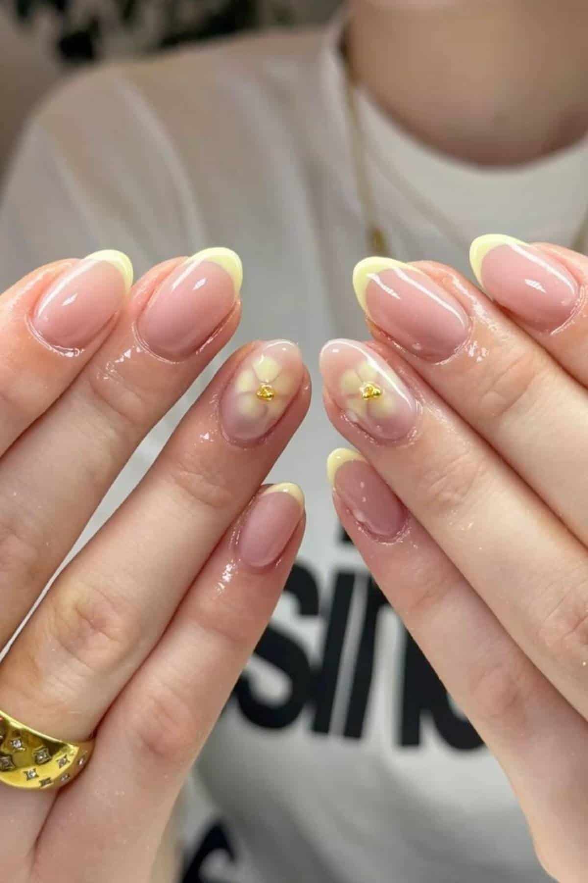Hands with pale yellow French tip nails; two accent nails feature a clear flower design with a small gold bead in the center.