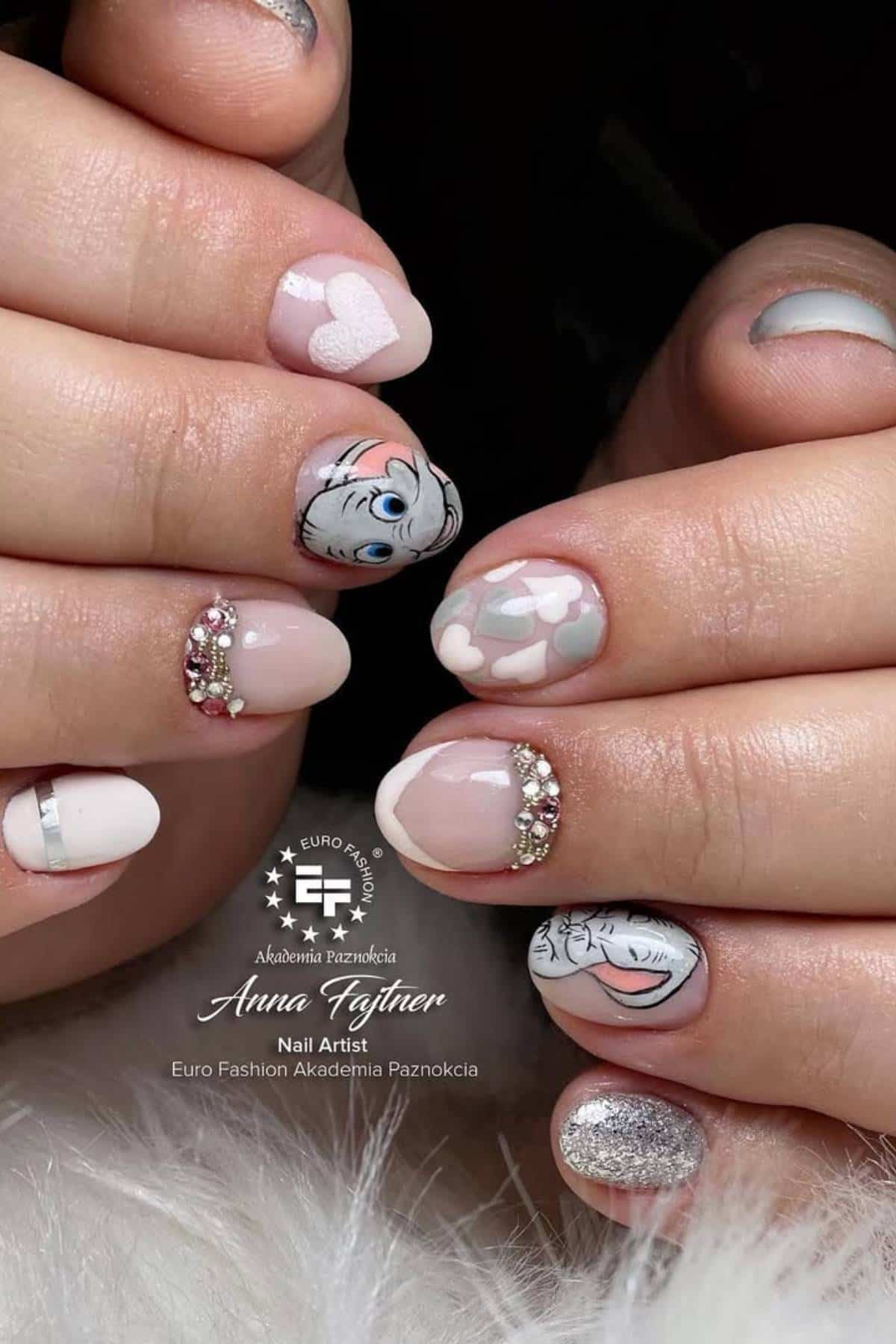 Close-up of manicured hands with light pink and white nails, featuring heart shapes, rhinestone accents, and cartoon character art.