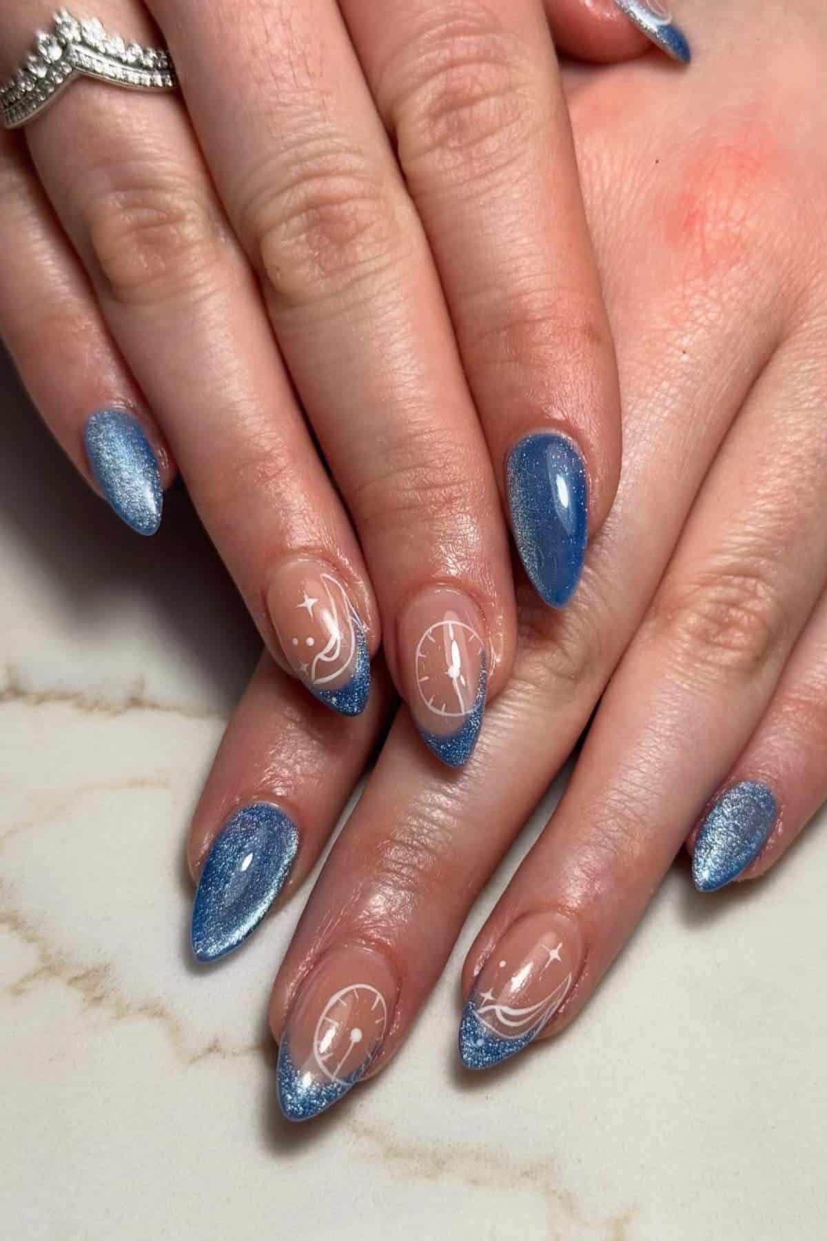 Hands with blue glittery French tip nails, featuring white designs such as stars, clocks, and glass slippers on some nails.