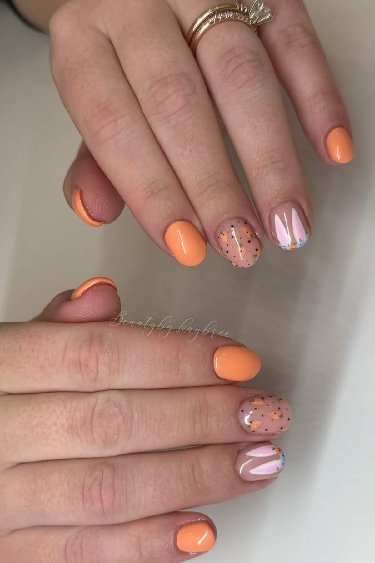Hands with short nails painted in orange and nude polish; accent nails feature glitter and colorful confetti designs.