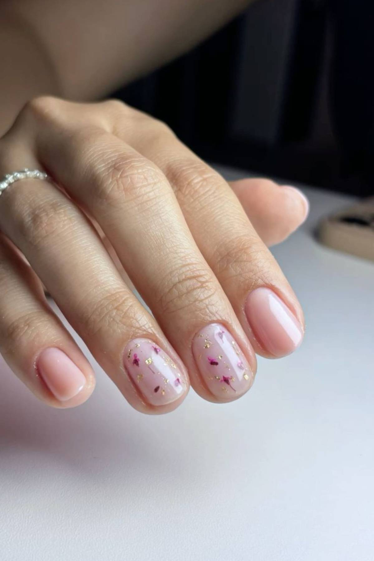A hand with short, neatly manicured nails painted light pink; two nails feature gold and pink foil accents.