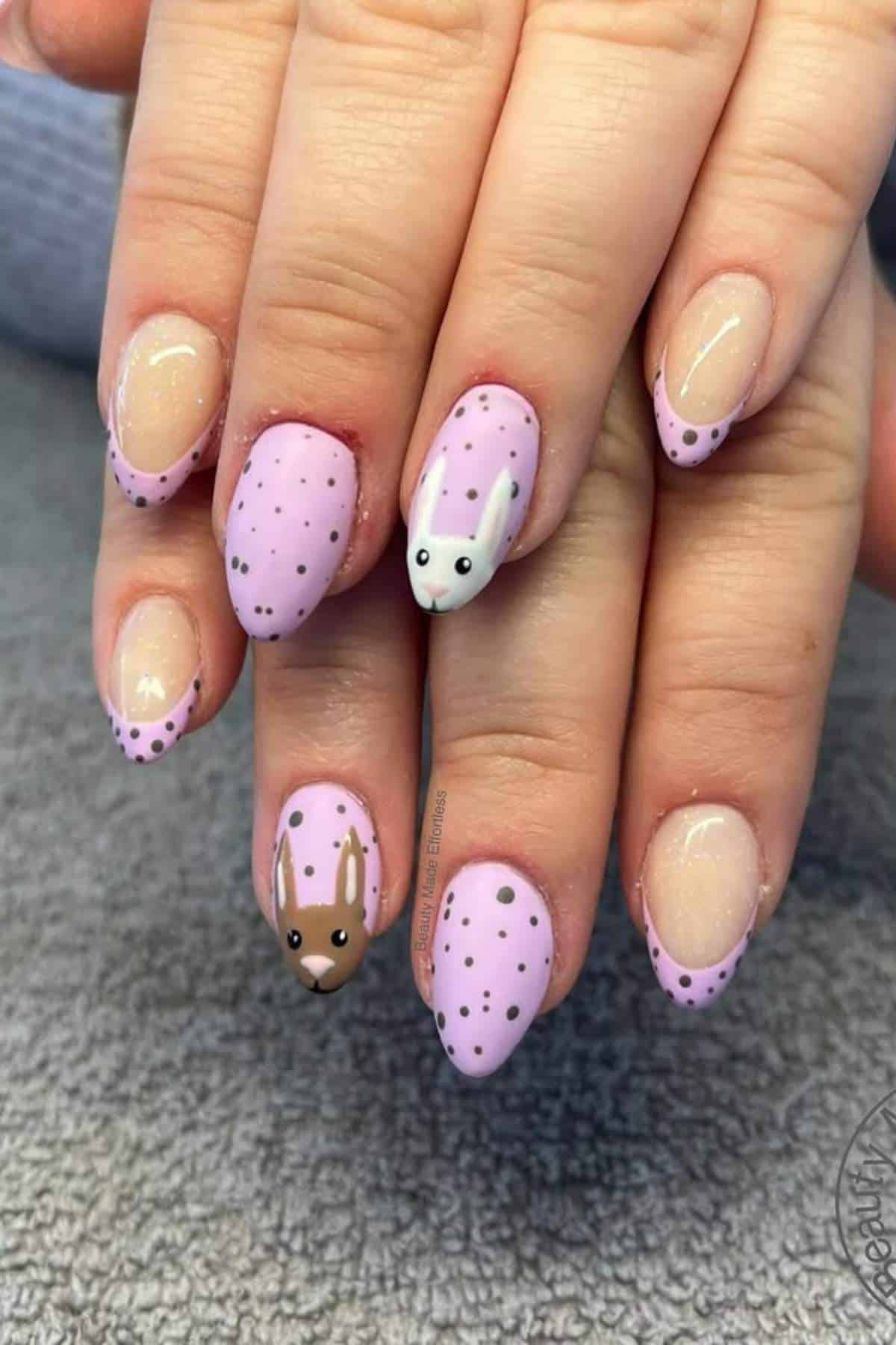 Hands with almond-shaped nails painted pink with black dots; two nails feature animal face designs, one resembling a rabbit and the other a deer.