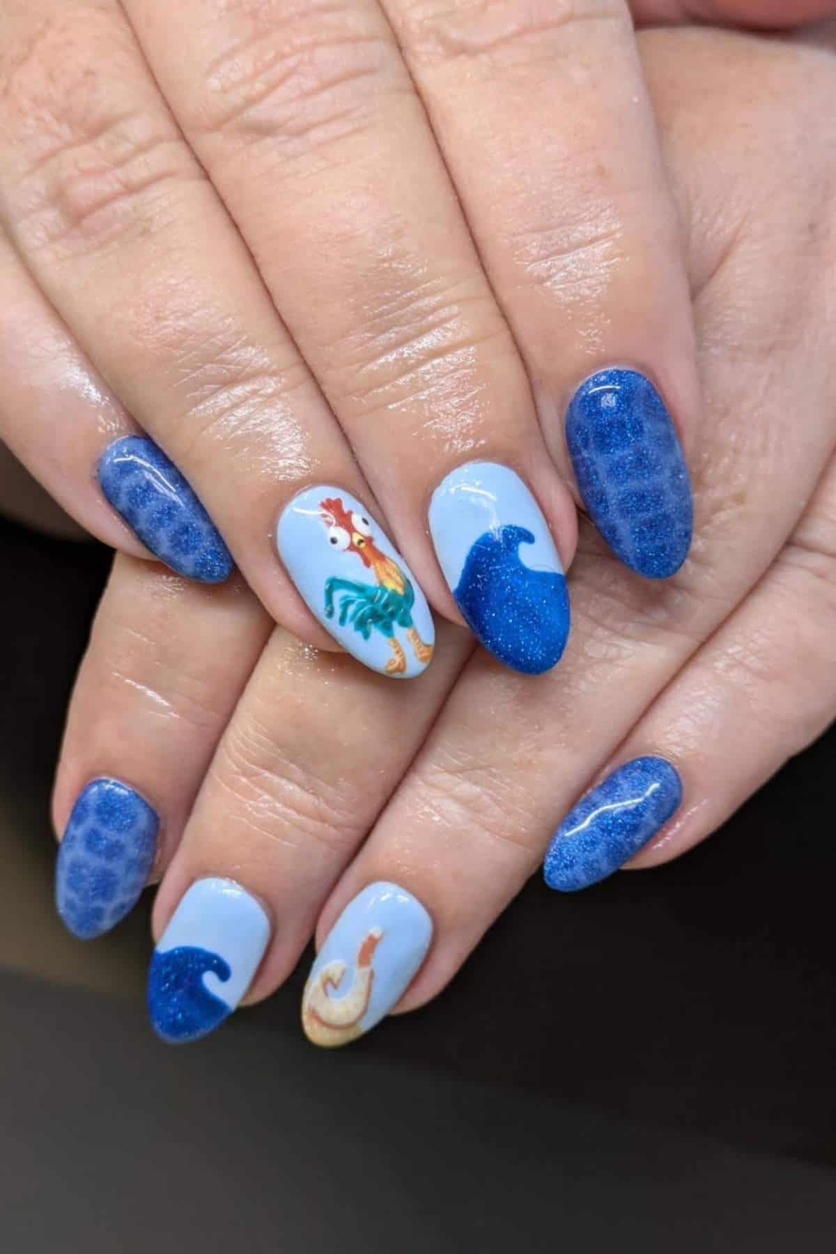 Hands with blue and light blue nail art featuring ocean waves, a rooster on one nail, and a seashell on another nail.