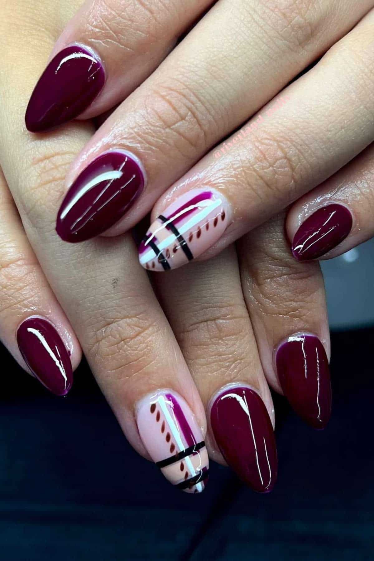 Hands with almond-shaped burgundy nails; ring fingers feature nail art with lines, dots, and geometric patterns in black, white, pink, and burgundy on a nude base.