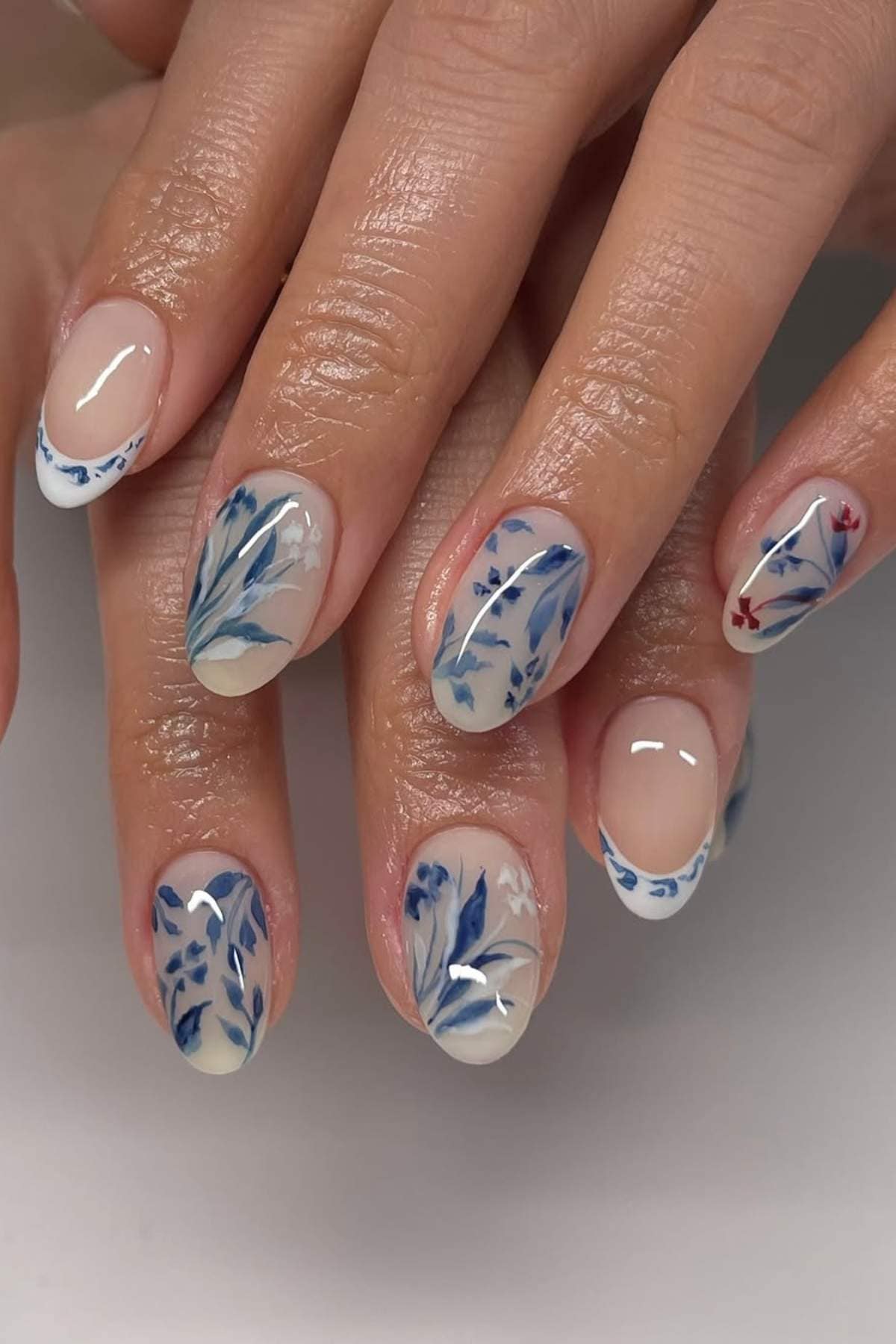 Close-up of hands with manicured nails featuring blue floral designs and delicate patterns on a neutral base.