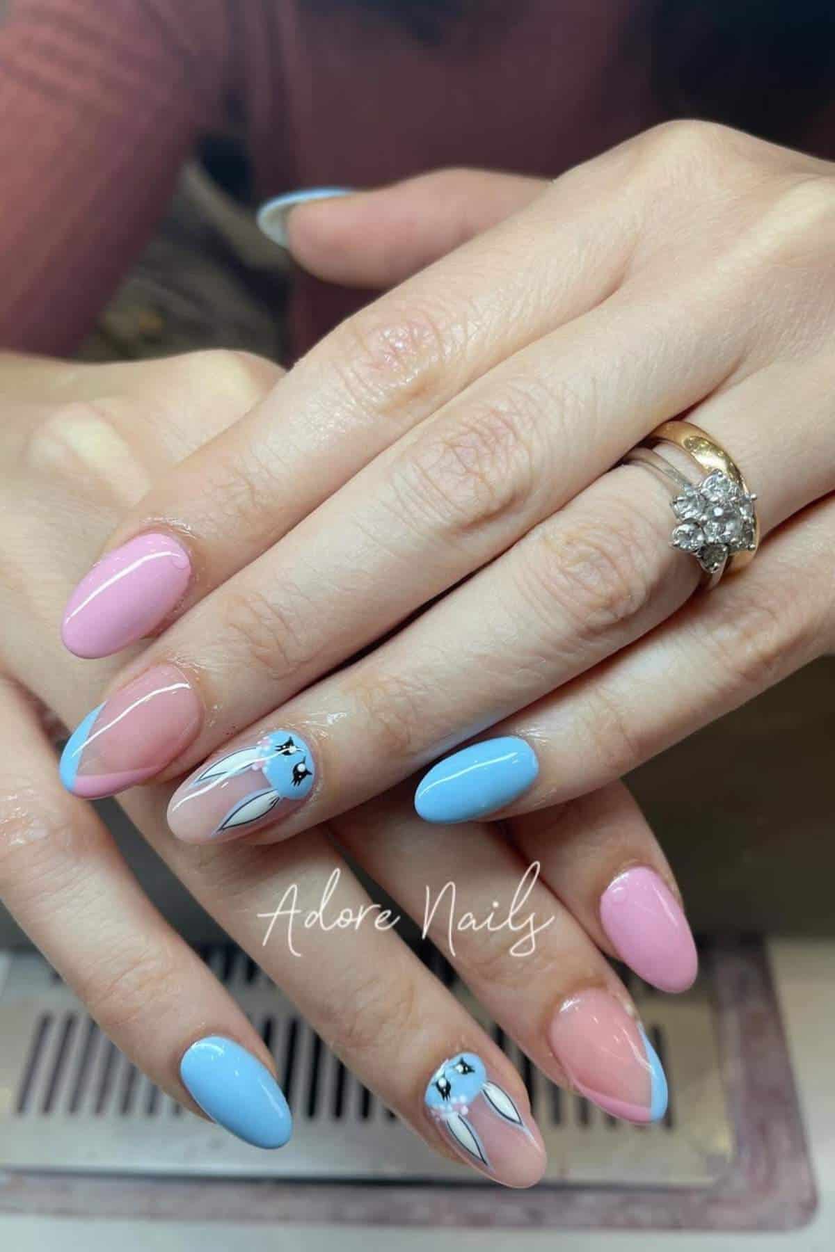 Close-up of hands with almond-shaped nails painted in pink and blue, featuring a bunny ear and star design on two accent nails.