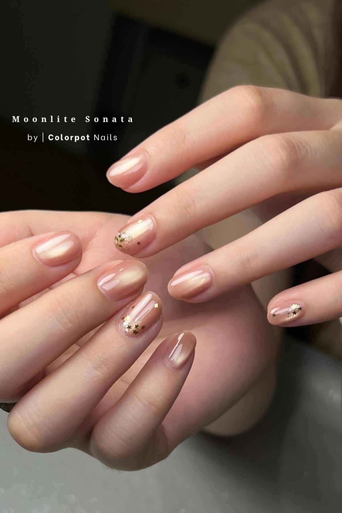 Close-up of hands with short, glossy nude nails featuring gold glitter accents on a few fingernails; text on image reads "Moonlite Sonata by Colorpot Nails.