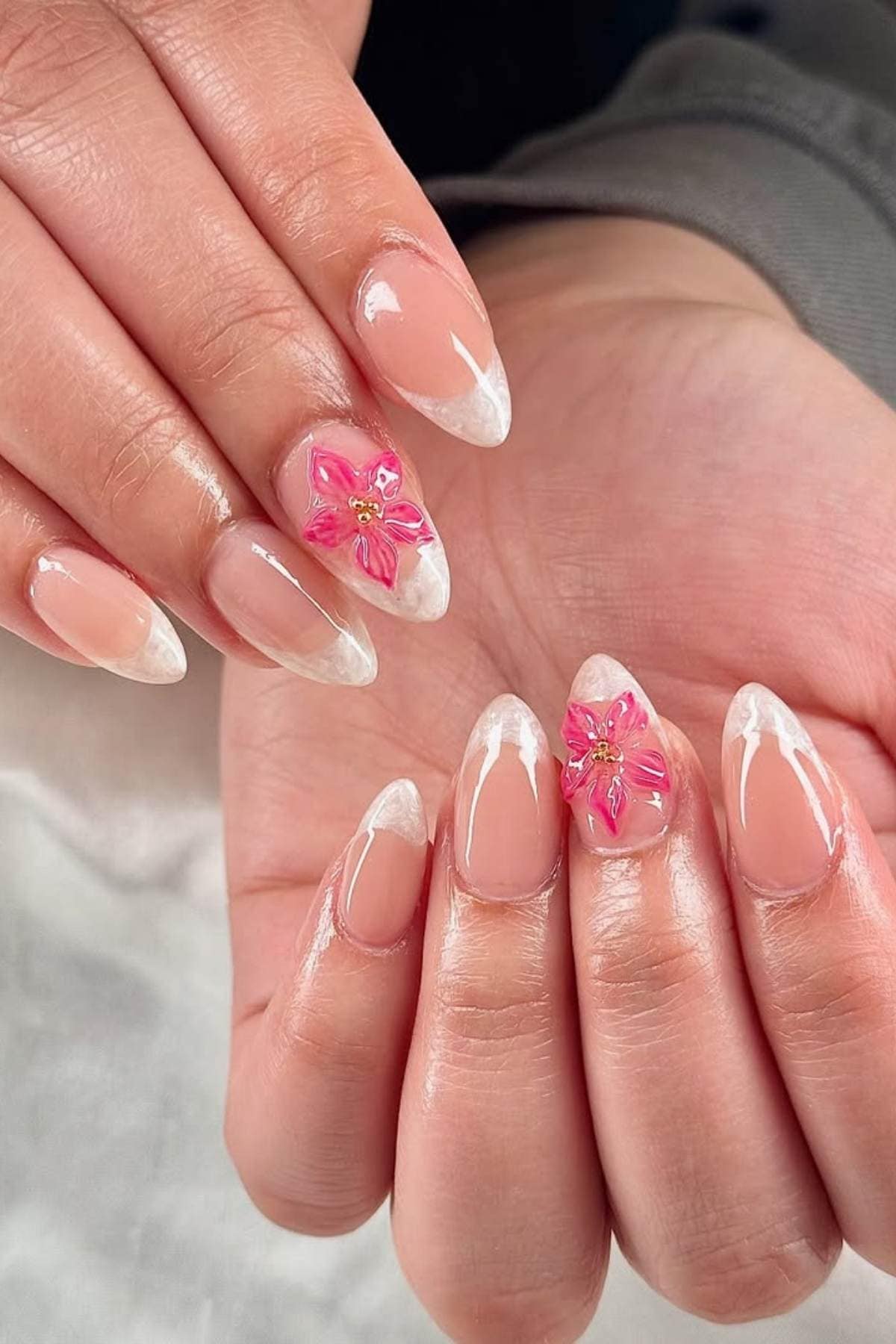 Hands with almond-shaped nails feature a natural pink base, white tips, and pink 3D floral designs with yellow centers on the ring fingers.
