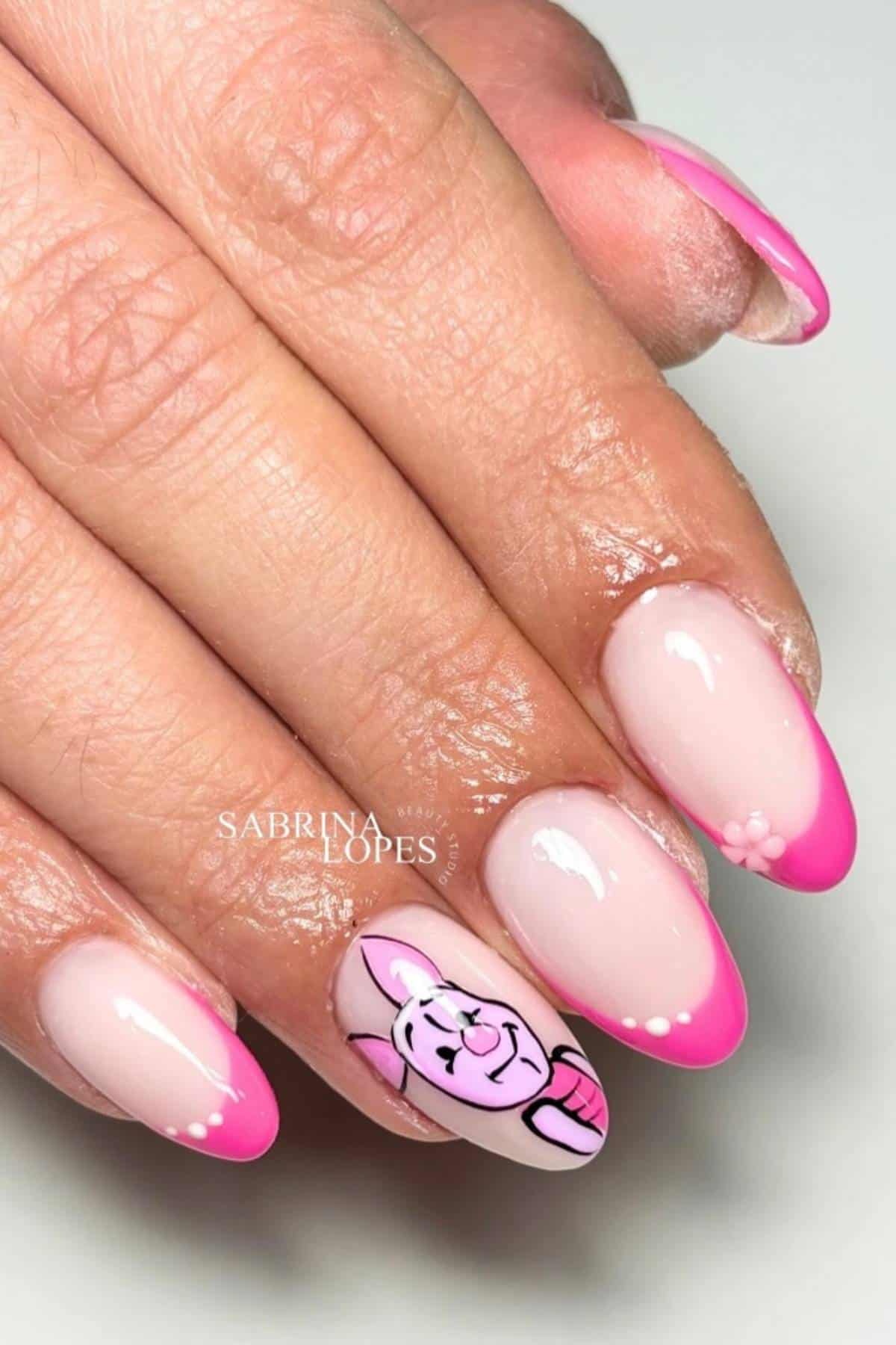 A hand with pink French tip nails, one featuring a cartoon pig face design and small white dot accents.