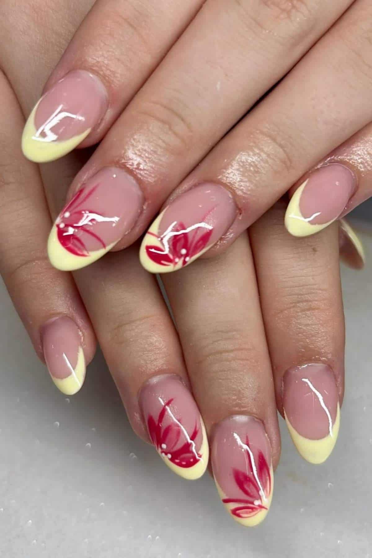 Hands with almond-shaped nails featuring pale yellow French tips and red and white floral designs on select nails.