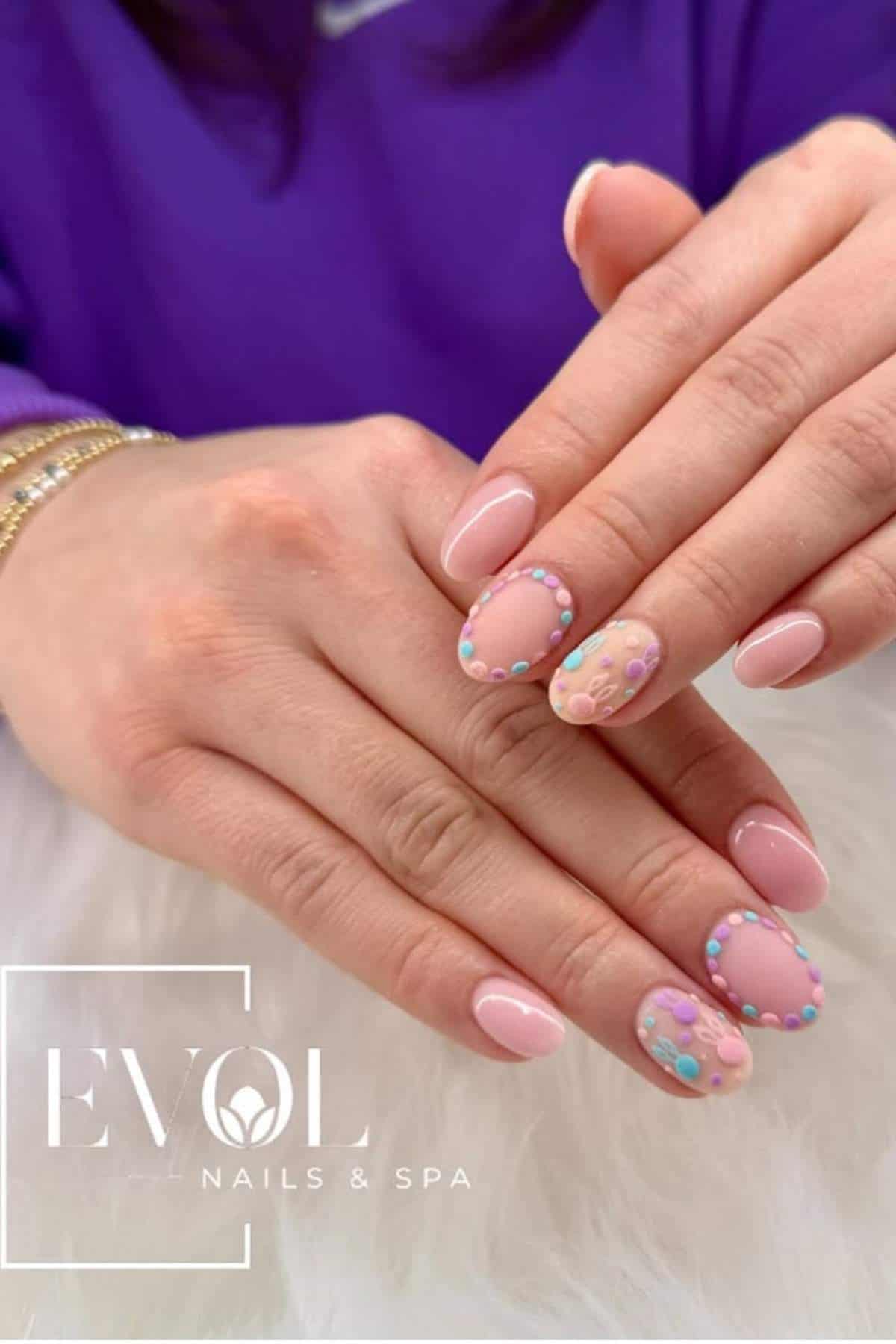 Hands with light pink manicured nails, featuring colorful 3D bead and floral designs on two accent nails. Logo reads "EVOL Nails & Spa.