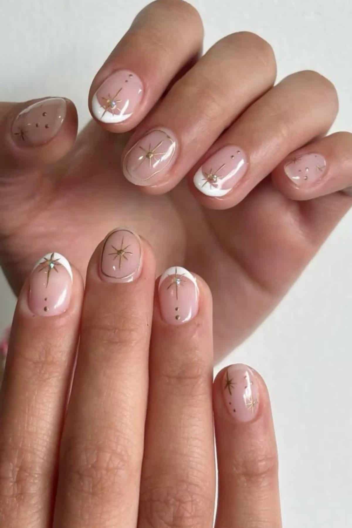 Hands with short, neatly manicured nails featuring a sheer nude base and decorated with small gold star and dot accents.
