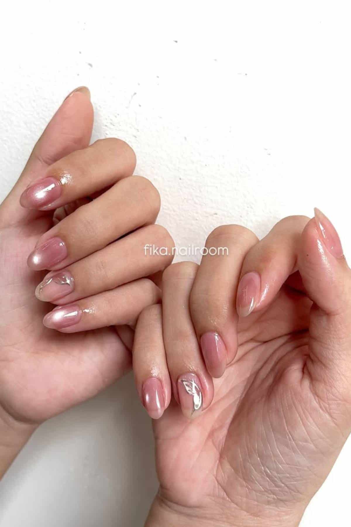Hands with natural-shaped nails featuring sheer pink polish and subtle white abstract designs on select nails, held against a plain white background.