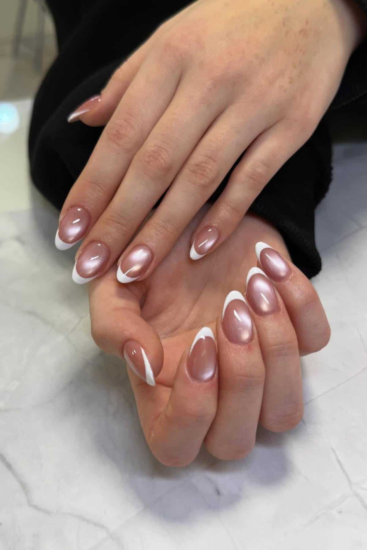 Hands with manicured nails featuring a glossy nude polish and white tips, displayed on a light marble surface.