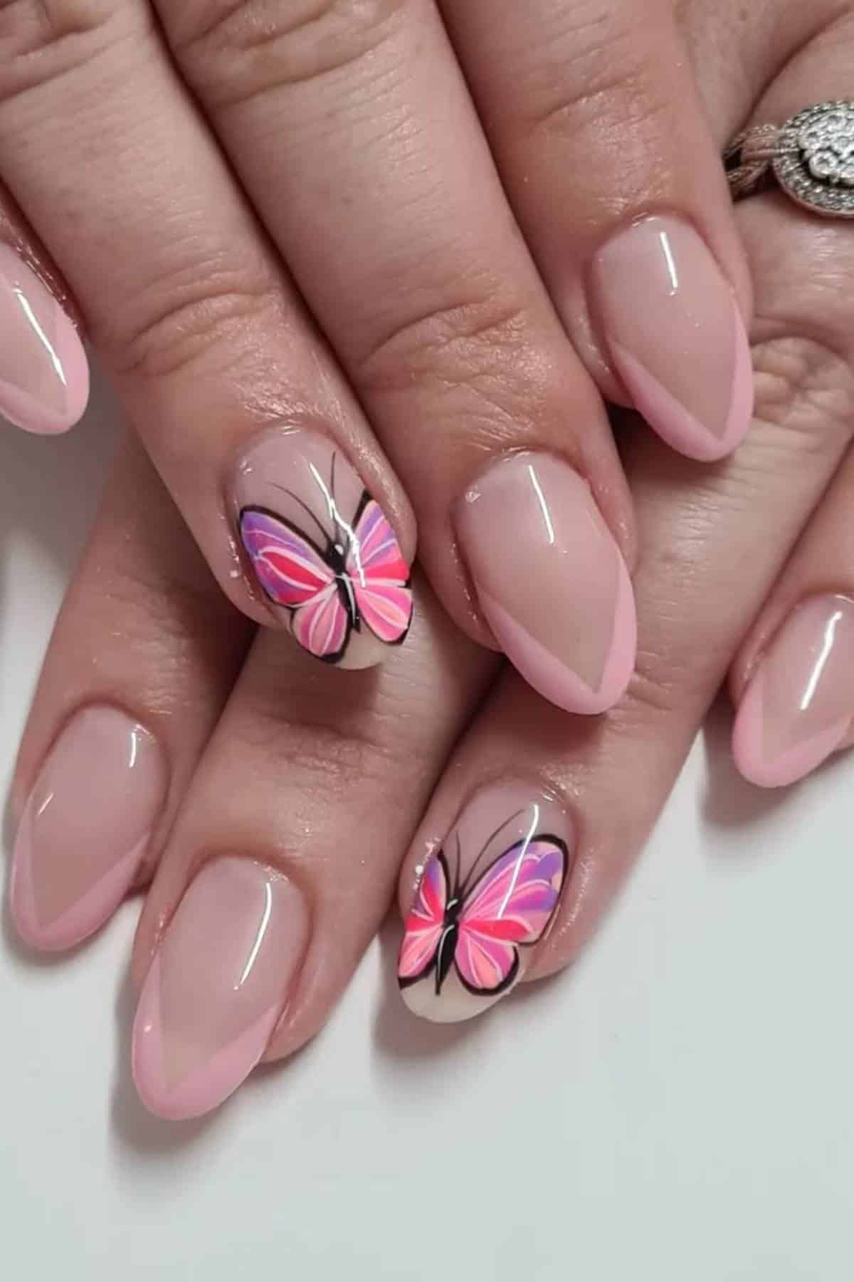 Hands with almond-shaped, light pink French manicure; the ring fingers feature detailed pink and purple butterfly nail art.