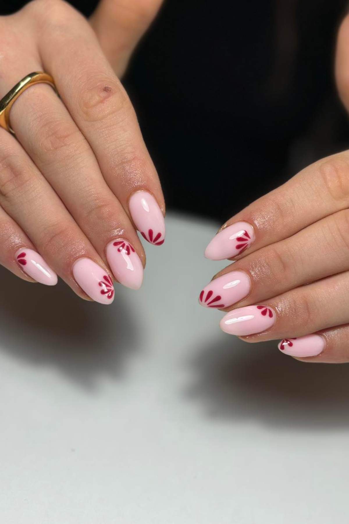 Hands with almond-shaped nails painted light pink, featuring red abstract floral designs near the cuticles.