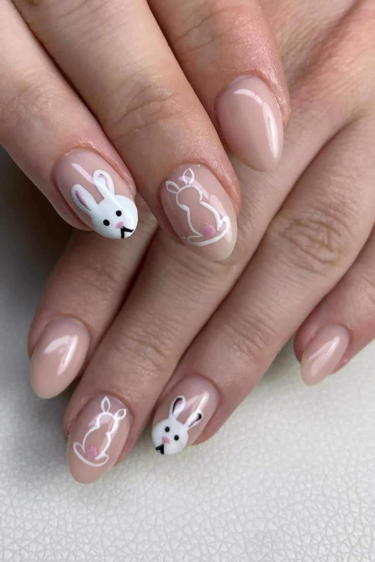 Close-up of hands with light pink nail polish and white bunny designs on two fingernails.