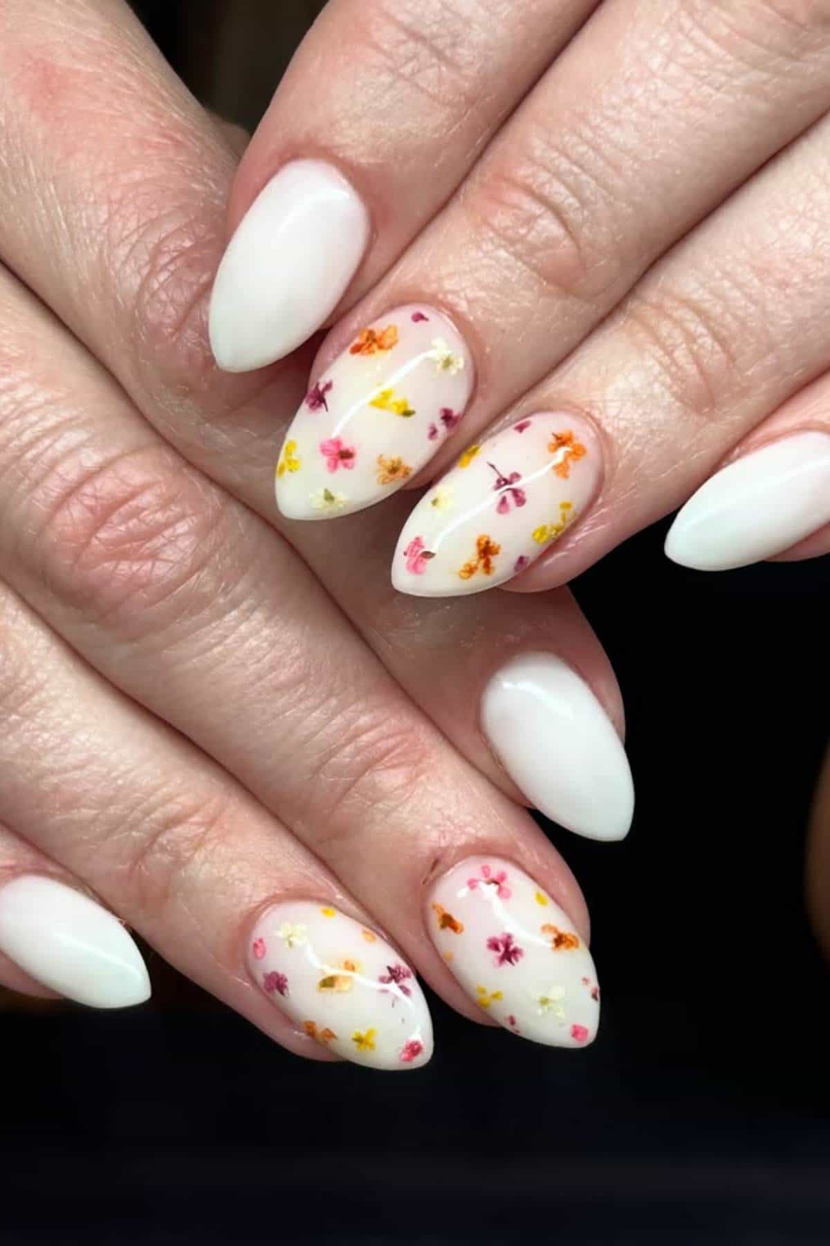 Hands with almond-shaped nails painted white; some nails have small, colorful floral designs.