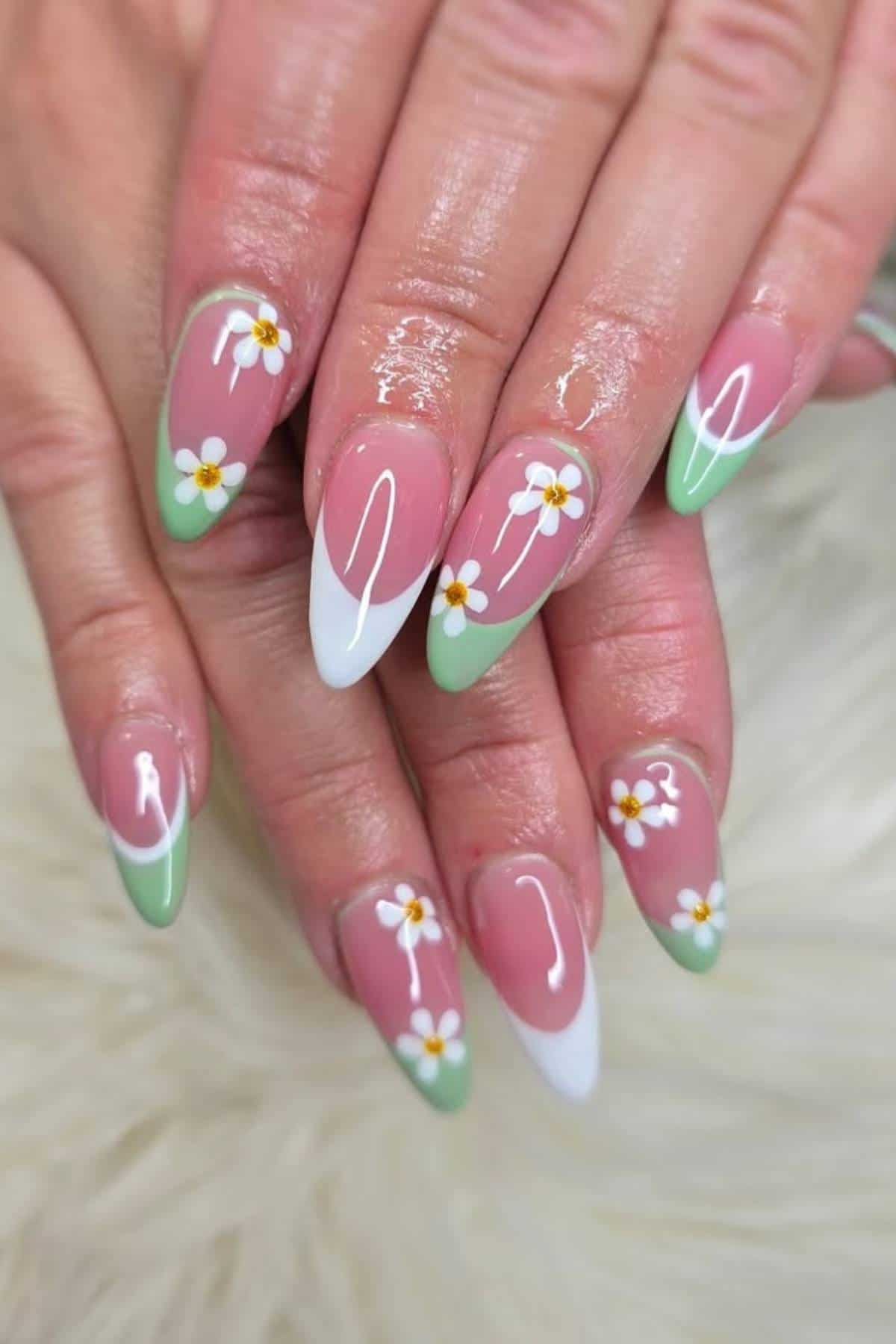 Hands with almond-shaped nails featuring a green and white French tip design, decorated with small white daisy flower accents and glossy finish.