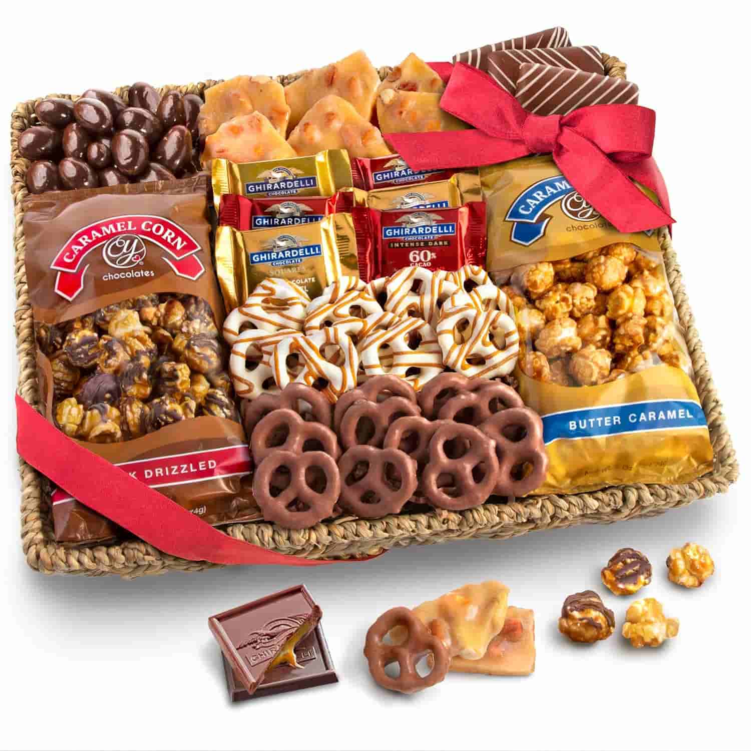 A gift basket filled with assorted chocolates, caramel popcorn, chocolate-covered pretzels, Ghirardelli chocolate squares, and brittle, decorated with a red ribbon.
