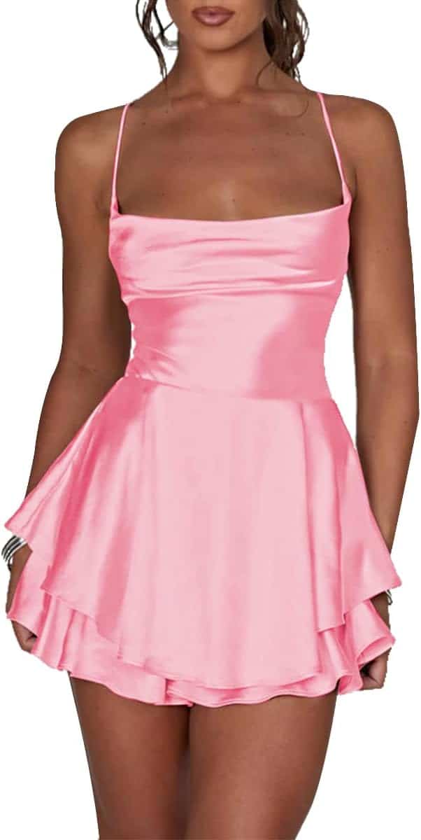 Woman wearing a sleeveless, pink satin mini dress with thin straps and a layered skirt, standing against a white background.